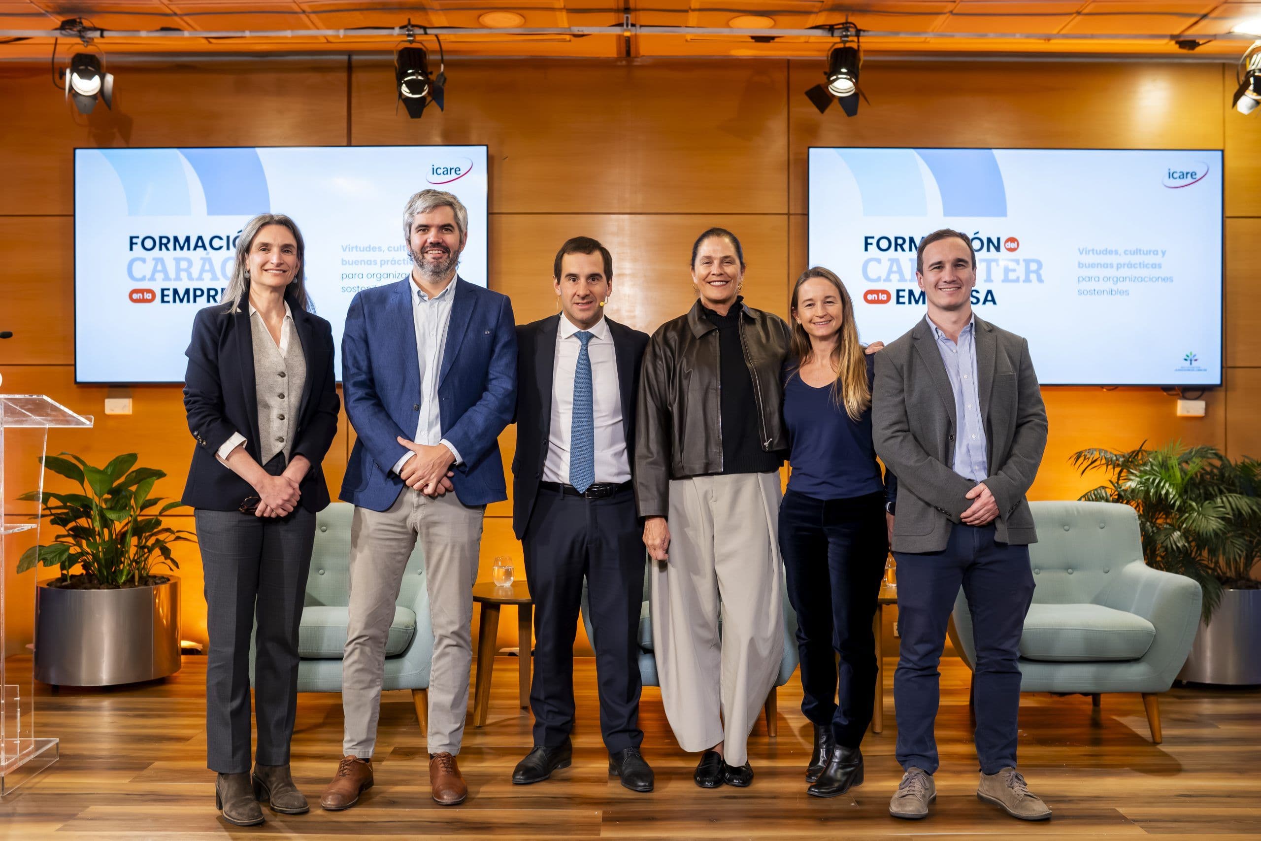 Six professionals pose in front of two large screens at a corporate event.