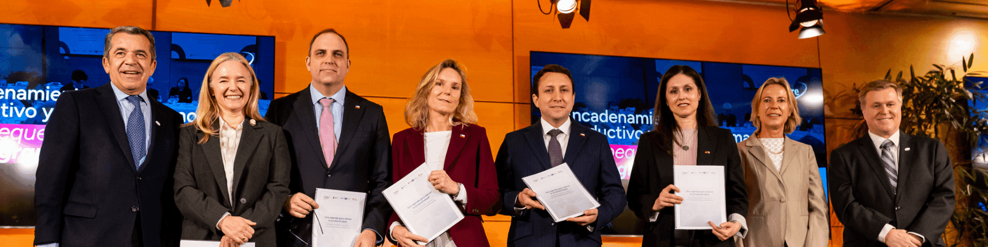 Nine officials, five women and four men, smiling and holding documents at a formal event.
