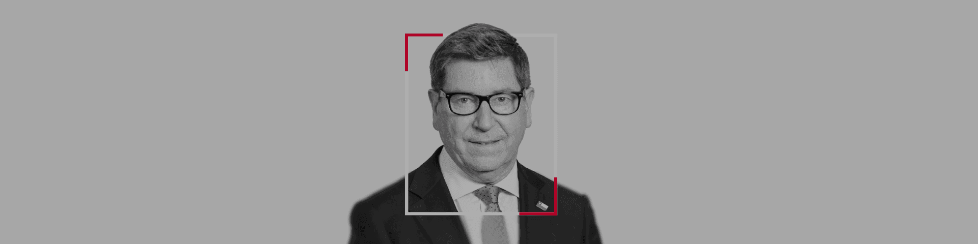 Black and white portrait of a smiling man in glasses, suit, and tie.